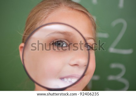 Close up of a schoolgirl looking through a magnifying glass in a classroom