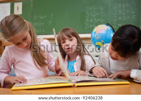 Cute schoolgirls reading a fairy tale to their classmate in a classroom