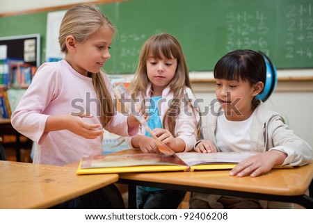 Little schoolgirls reading a fairy tale to their classmate in a classroom