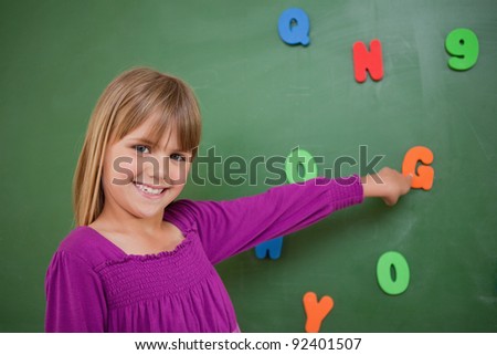 Little schoolgirl pointing at a letter in a classroom