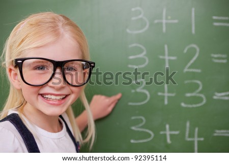 Smart schoolgirl pointing at something on a blackboard