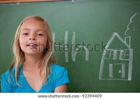 Blonde schoolgirl posing in front of a blackboard in a classroom