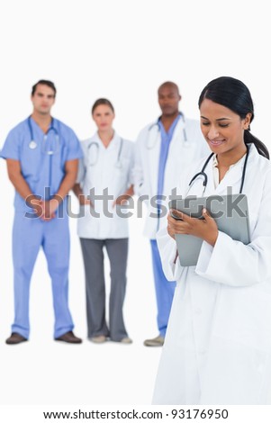 Female doctor taking notes with staff members behind her against a white background