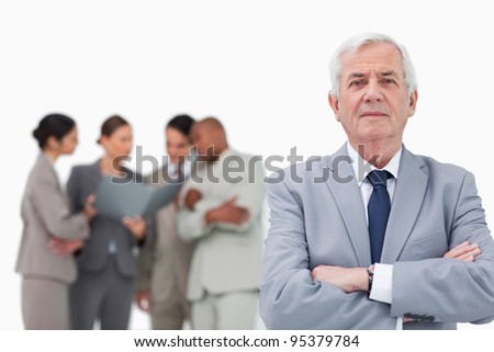 Mature salesman with arms folded and team behind him against a white background