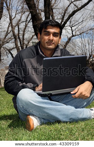 Young Indian student working on his laptop outside the college campus.