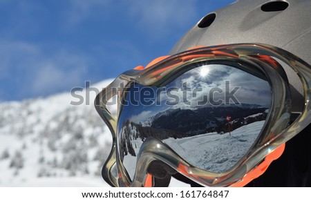 Winter mountain landscape and ski slope reflected in a ski mask. \
Selective focus.