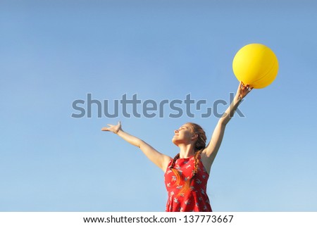 Girl in red dress whith sun yellow baloon on a sky background