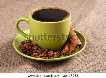 Green cup of coffee with beans on background