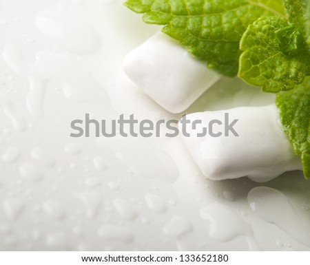 Two chewing gums with fresh green mint leaves background