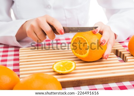 female chef cuts oranges on white background