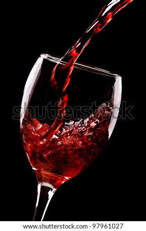 red wine pouring into wine glass isolated on a black background