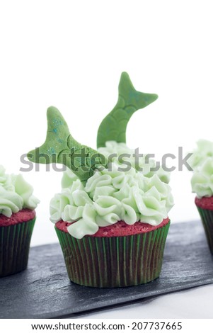 Tasty cupcakes with green icing and fish tails decoration on a shale tray