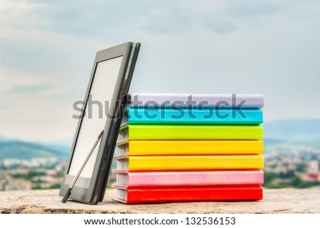 Stack of colorful books with electronic book reader against blue sky