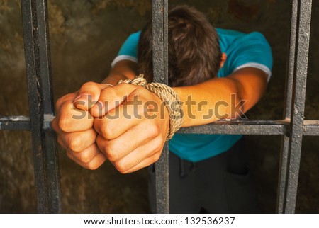 Man behind the bars with hands tied up with rope