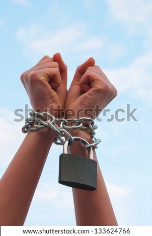 Woman\'s hands tied up with chains against blue sky