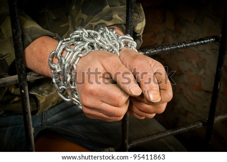 Hands of man tied up with chain behind bars