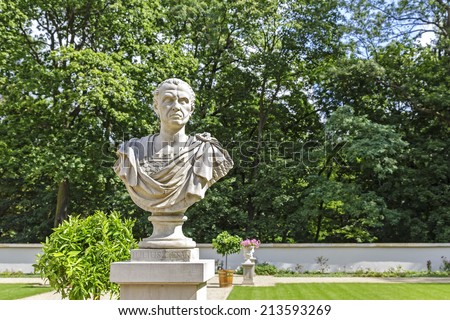 WARSAW, POLAND - AUGUST 25, 2014: Bust of Julius Caesar, one of Rome\'s most famous statesmen, politicians and generals, located  in a garden with sculptures in front of the Old Orangery