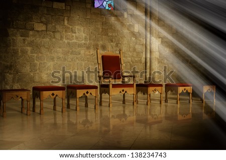 Throne with antique wooden chairs in a dark room with an old stone wall in the background and the rays of sunlight falling from a window, a symbol of power and ruling