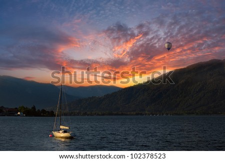 Colorful sunset on Lake, with yacht on water and air baloon in the sky, Alps mountains on background