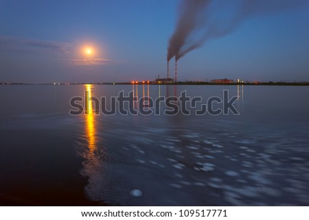 Power station in the evening, with lights and smoke reflection in water, full moon, long exposure