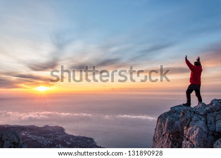 A man standing at mountain top with open arms set against a beautiful sunrise, feeling freedom