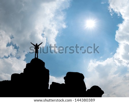 Happy man standing at mountain top with open arms, sun in blue sky on background