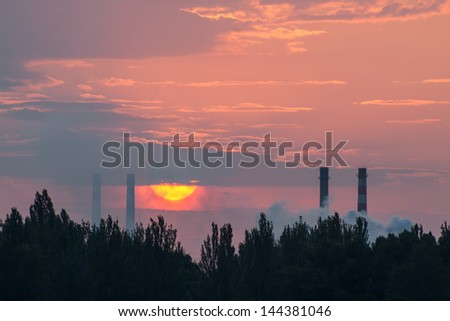 The sun sets between the pipes from which the smoke coming, industrial landscape