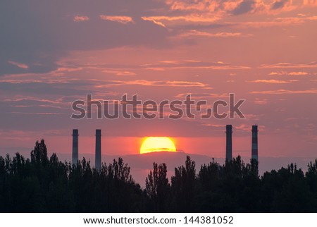 The sun sets between the pipes from which the smoke coming, industrial landscape