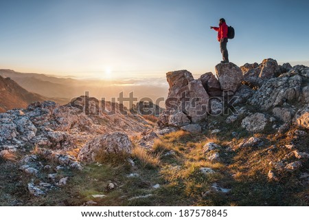 A happy traveler on a mountain top looking ahead. Shows his hand toward the horizon
