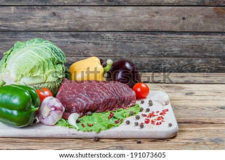 Raw meat, spices and vegetables on rustic wooden board