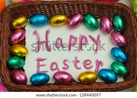 Hand drawn easter greeting message on the bottom of easter basket, surrounded with chocolate easter eggs;