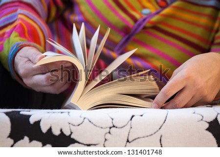 Woman in colorful blouse lying on black and white sofa while reading book