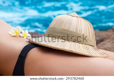 Woman lying on the beach with straw hat and frangipani flowers on her belly