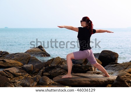 Woman doing yoga on the rock and looking at sea. Pose warrior II