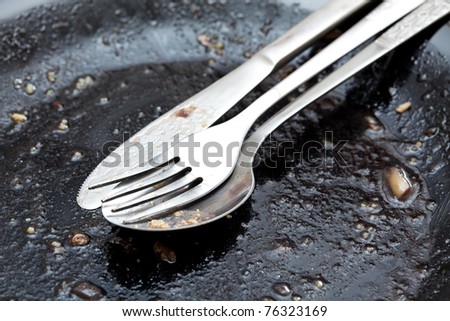 Close up of dirty spoon, fork and knife on black plate