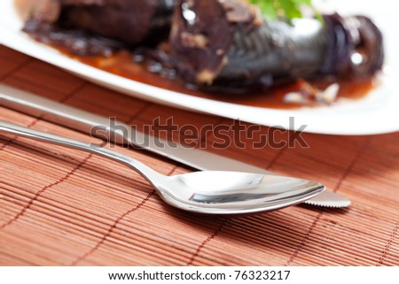 Close up of spoon and knife on bamboo tablecloth next to plate with tasty Mediterranean meal \