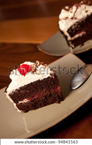 Black forest cake on a dark plate with a maraschino cherry and spoonBlack Forest Cake with maraschino cherry