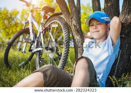 happy kid with a bicycle resting under a tree