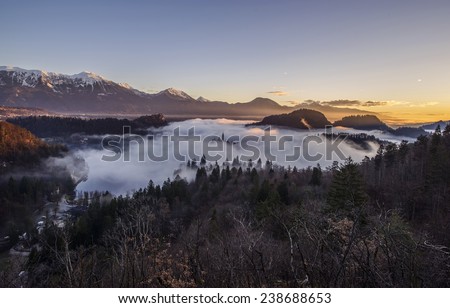 Mystical Sunrise over Lake in the Mountains. Mist is over the lake covering the church almost in full. Castle and surrounding Mountains are basking in the sun. Scenic and atmospheric sunrise on Bled.