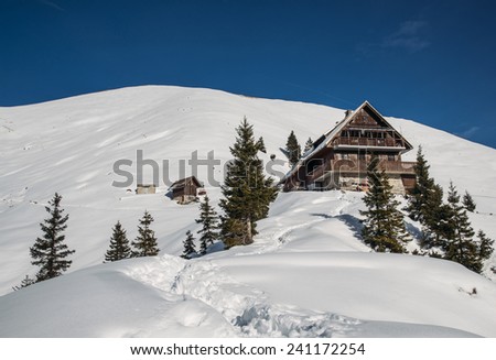 Hiking in the winter hills and mountains. Outdoor activity on a clear and sunny day. Vast forests and meadows covered with snow. Dramatic scenery in the Julian Alps. Mountain cottage with trees.