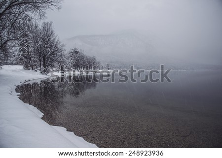 Reflection of the landscape in the lake. Winter Fairytale at Bohinj Lake in Slovenia. Mystical landscape on a winter day with heavy snow. Cottages reflection in the Snow.