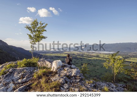 Man standing at the top of the hill and taking photos of the picturesque valley below. Vivid colors of the meadows and fields.