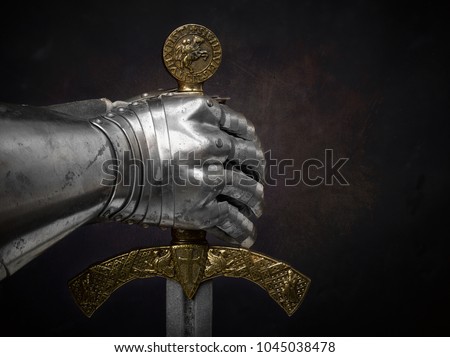 A beautiful ancient sword of the Order of the Knights Templar and an iron knight\'s glove on a dark beautiful background.