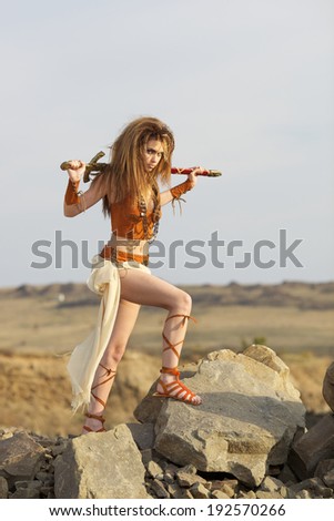 The beautiful girl with a sword in a suit of the amazon costs on a stone height