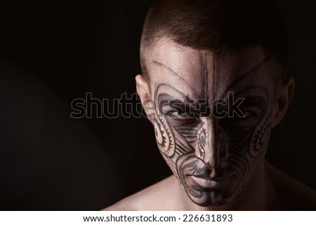 Beautiful man\'s portrait with the ornament drawn on a face and jewelry on a black background