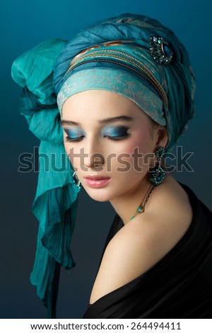 Romantic portrait of young woman in a turquoise turban with jewelry on a beautiful background