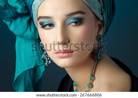 Romantic portrait of young woman in a turquoise turban with jewelry on a beautiful background