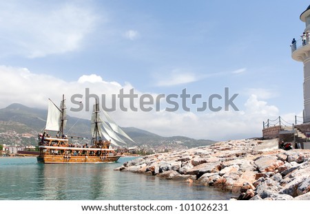 Tall wooden vintage sailing ship next to light house