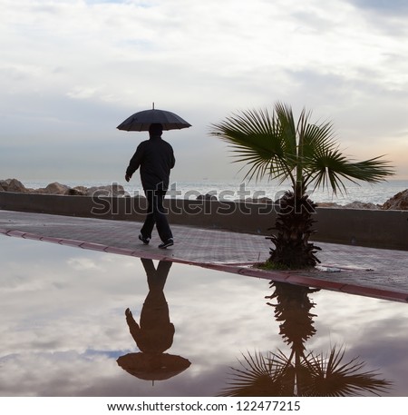 Lonely man walking with umbrella under the rain