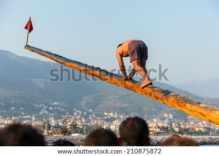 ALANYA -TURKEY - JULY 01: man showed in the coast in Alanya beach for Feast of cabotage on july 01, 2014 in Alanya Turkey.  Man walks over oily wooden pole and trying to take the flag